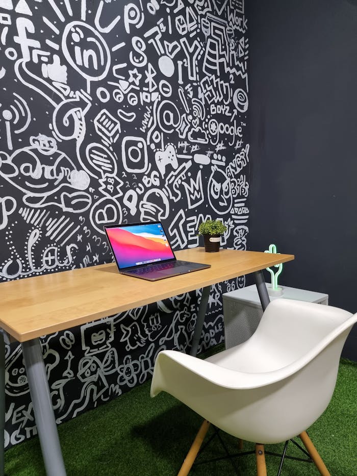Contemporary office setup featuring a laptop on a wooden desk against a graffiti wall.